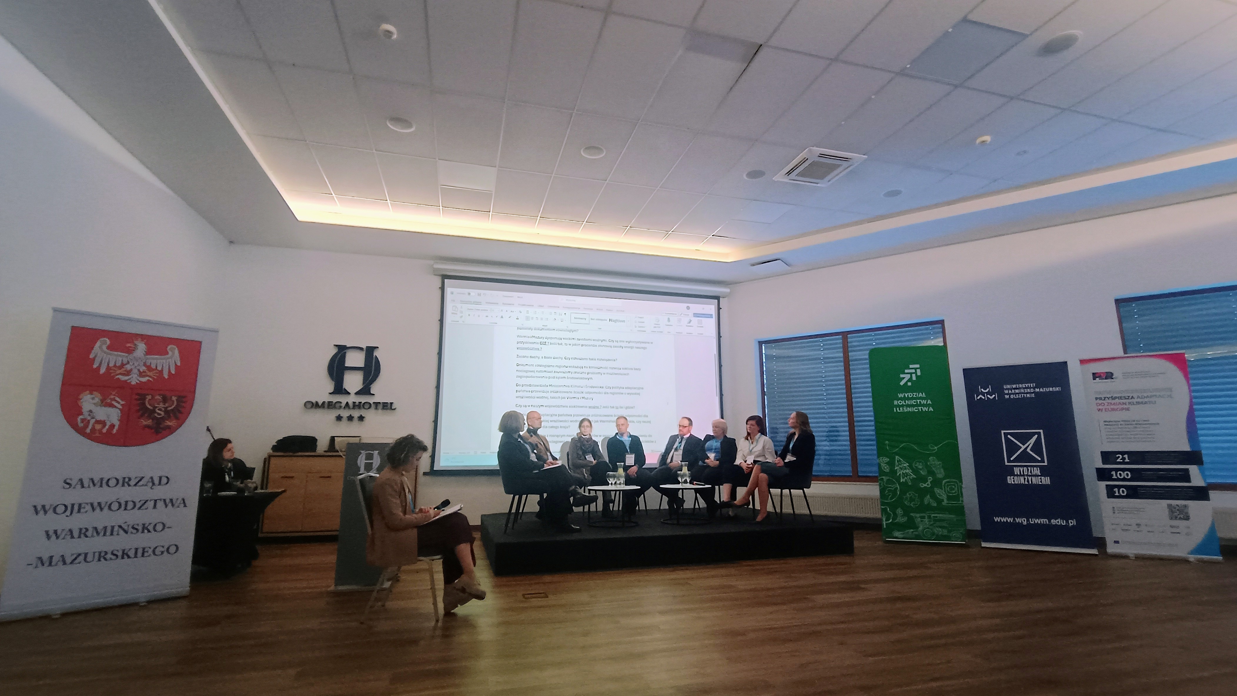 Na zdjęciu widoczna jest scena na której siedzą osoby uczestniczące w debacie podczas konferencji.